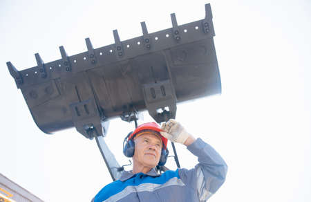 Excavator driver in hard hat stands at construction equipment, concept industrial man portraitの写真素材
