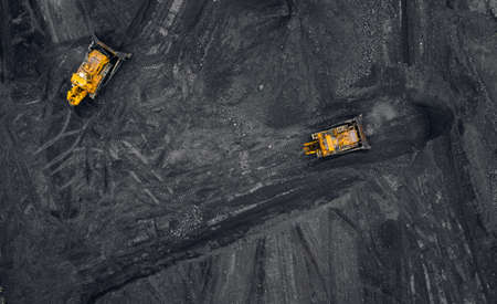Loading coal, two yellow excavators handling anthracite in an open mine, aerial top viewの写真素材