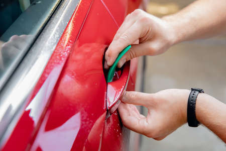 Closeup master installation on in risk zone under handles red car. Paint protection is vinyl filmの写真素材