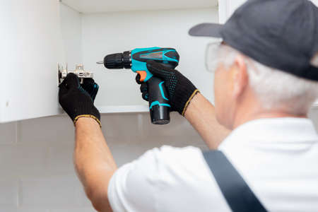 Worker man in uniform installs fittings assembling furniture in kitchenの写真素材