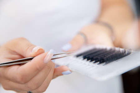 Eyelash extension master holds tweezers and palette of materials in his handsの写真素材