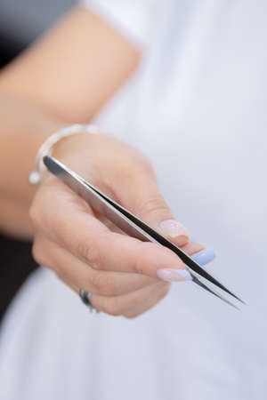 Closeup Eyelash extension master holds tweezers in handsの写真素材