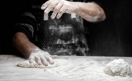 Hands baker preparing yeast dough with white dust flour on black background, scoop for pasta and...
