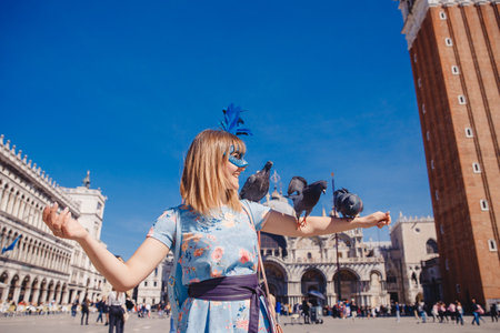 Portrait smiling young woman in Venice, Italy in Venetian mask feeds pigeons on St Mark Square. Concept travelの写真素材