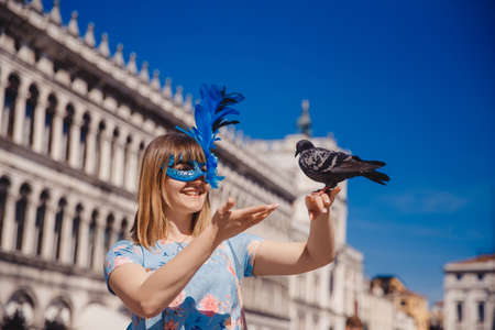 Portrait smiling young woman in Venice, Italy in Venetian mask holding pigeons on St Mark Square. Concept travelの写真素材