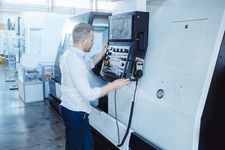 Young male engineer operating CNC machinery in iron metal factoryの写真素材