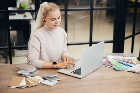 Happy young woman is online education interior design course behind laptop. Concept choosing profession of Internet designerの写真素材
