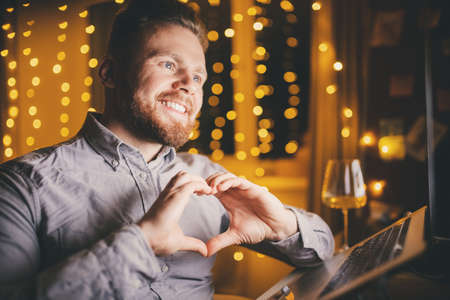 Lover man online video call on laptop, hands sign heart. Concept remote virtual dating distance during quarantine Covid-19の写真素材