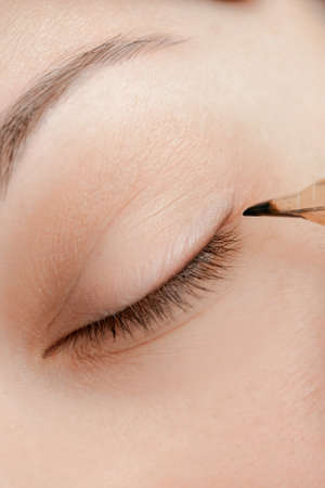 Master makes permanent tattoo makeup on eyelashes of eyes of young woman in beauty salonの写真素材