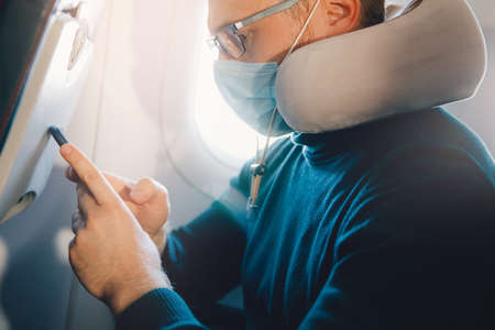 Man use phone in airplane during flight wearing face mask. Concept personal protection in travelの写真素材