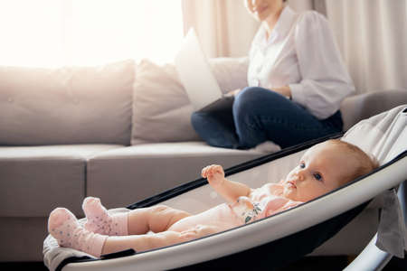Beautiful young mother with baby girl working at home office using laptop computer, sun light. Concept freelance life style maternity leaveの写真素材