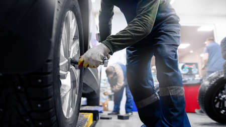 Concept car service replacement of winter and summer tires. Mechanic holding wheels at garageの写真素材