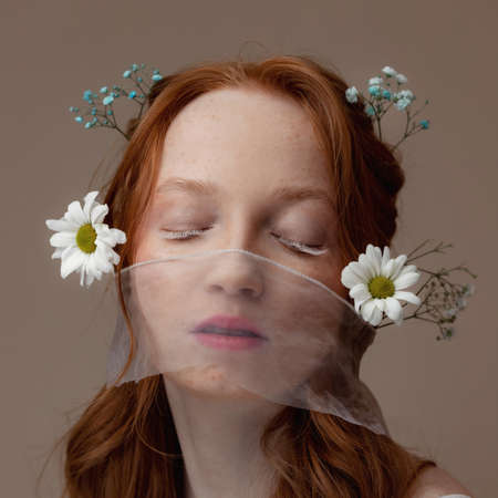 Concept bio cosmetics, eco skin care girl. Spring fashion portrait of young woman with chamomile flowers in red hair with white lashの写真素材