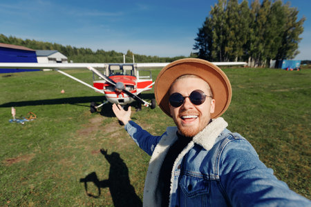 Concept travel trip private aviation. Selfie photo happy tourist man pilot in hat and glasses background white aircraft cockpitの写真素材