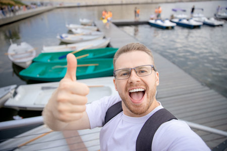 Happy male traveler makes selfie photo on background of catamarans parking. Concept travel walk on...