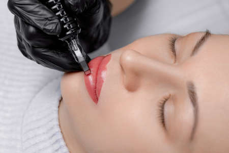 Process applying permanent makeup tattoo of red on lips woman in beautician salonの写真素材
