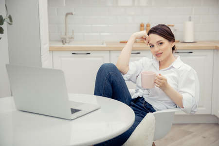 Woman working on internet with laptop at home office white kitchen with cup tea. Concept influencer bloggerの写真素材