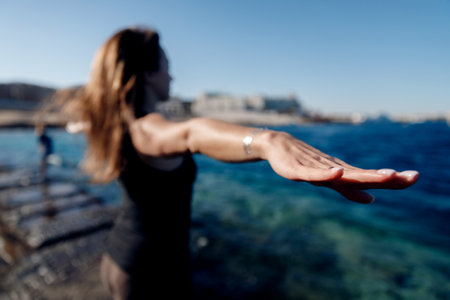 Concept freedom of female energy. Young woman practices yoga on background of sea, wind blows hairの写真素材