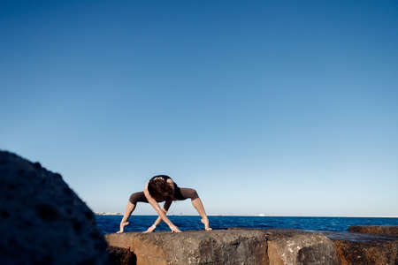 Concept woman power energy healthy life. Girl practices yoga on background of sea, wind blows hairの写真素材