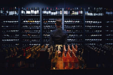 Blurred background for tasting, sommelier standing at wine shelf in liquor storeの写真素材
