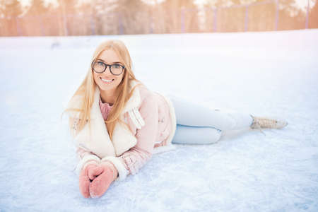 Happy young blonde woman in glasses posing on ice rink in winter, sunny flareの写真素材