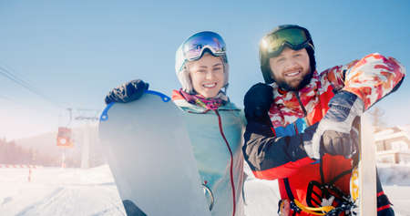 Happy young couple man and woman snowboarders on background of ski resort sun day. Concept Banner winter sport travelの写真素材