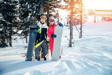 Concept friends travel love winter sport. Happy couple man and woman snowboarders background sunset ski resortの写真素材