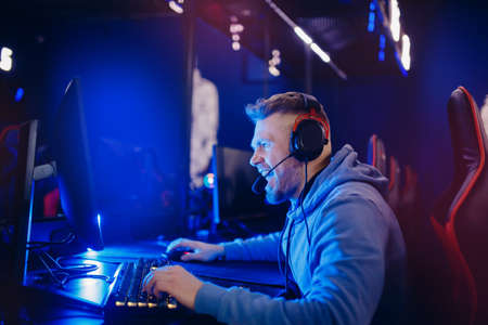 Streamer young man rejoices in victory professional gamer playing online games computer with headphones, neon colorの写真素材