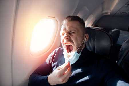 Afraid of fear flying on airplane and height tourist man in safe medical mask. Concept aerophobia or aviophobiaの写真素材