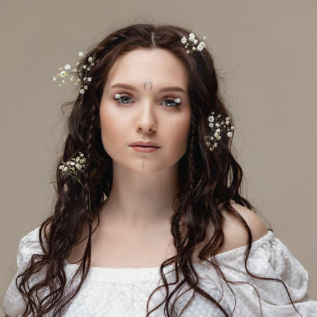 Portrait young beautiful woman with white flowers on eyes and hair. Spring fashion photo and skin care eyelashの写真素材