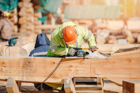 Industrial work carpenter grinds log with electric jointer, construction frame building site of house made of woodの写真素材