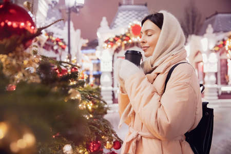 Happy young woman with cup hot coffee, Christmas market with bokeh light evening. Winter vacations in Red square Moscow, Russiaの写真素材