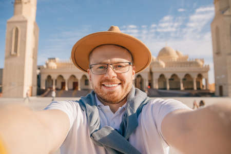 Tourist man in hat takes travel selfie photo background El Mina Masjid mosque in Hurghada, Egypt sunlightの写真素材