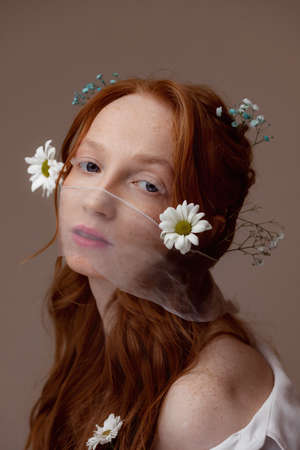 Concept bio cosmetics, eco skin care girl. Spring fashion portrait of young woman with chamomile flowers in red hair with white lashの写真素材