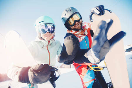 Happy young lover couple man and woman snowboarders on background of ski resort, sun lightの写真素材