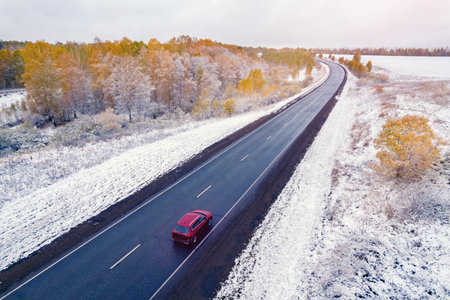 Red car rides winter road through forest, trees with snow, aerial top view droneの写真素材