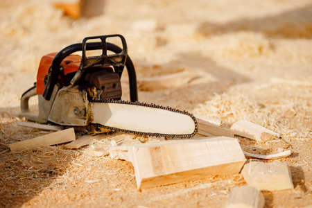 Chainsaw at construction site of wooden houses made of logs lies on background of sawdustの写真素材