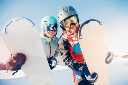 Smiling couple woman and man with snowboards background snowy mountain ski resort, sunny day sunlight. Concept travel winter sportsの写真素材