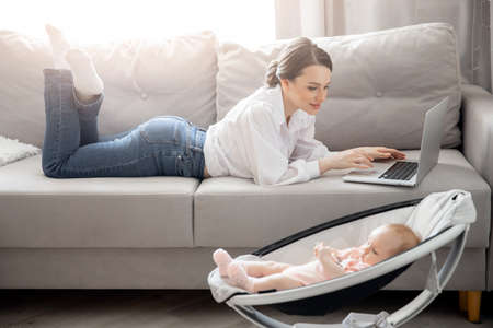 Businesswoman working at home office using laptop computer with baby, sun lightの写真素材