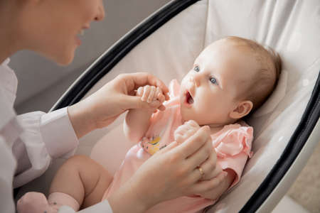 Mom holds little infant daughter by hand in automatic cradle for sleeping, sun light. Concept Morning with newborn babyの写真素材