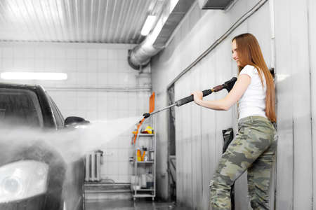 Car washing service. Worker woman cleaning auto using high pressure waterの写真素材