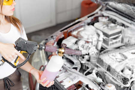 Service car wash, woman master spray foam to clean engine from dirtの写真素材