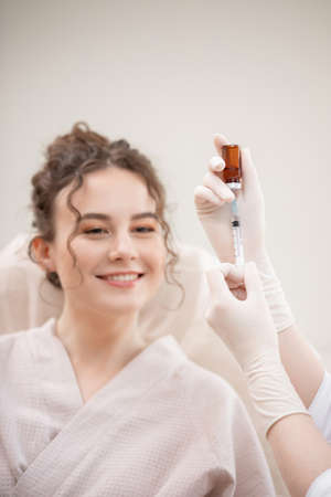 Correction of mimic wrinkles, shape of eyebrows and lips in young curly woman in beauty salon using filler and syringeの写真素材