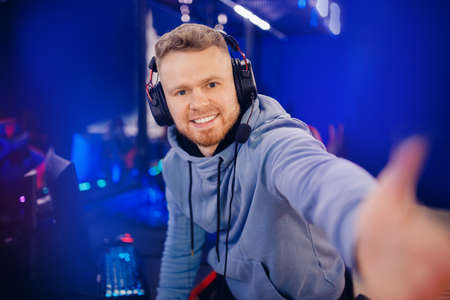 Streamer young man professional gamer playing online games computer with headphones make selfie photo, neon colorの写真素材