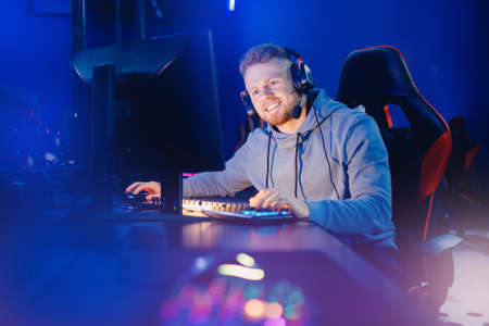 Streamer young man on chair in game studio. Gamer playing action video tournament online in dark room neon colorの写真素材