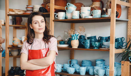 Confident young woman standing in an apron for pottery wheel. Concept of opening your own businessの写真素材