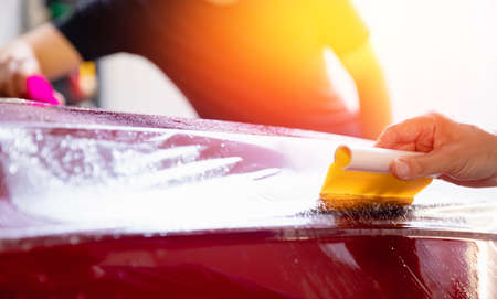 Process of pasting hood of red car with protective vinyl film from gravel chips and scratches. Transparent protection for paintの写真素材