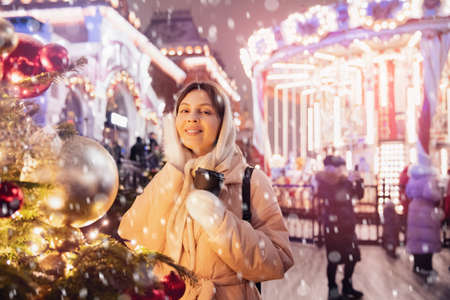 Happy young woman with cup hot coffee, Christmas market with bokeh light evening. Winter vacations in Red square Moscow, Russiaの写真素材
