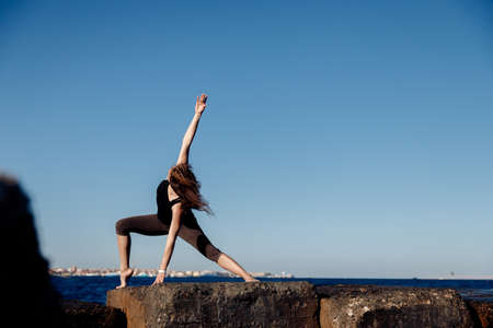 Girl practices yoga on background of sea and blue sky, wind blows hair. Concept solitude of woman and nature, selfacceptance, inner harmonyの写真素材