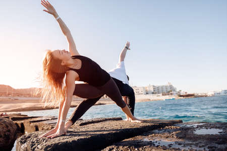 Couple woman and man doing asana yoga background sea and blue sky sunlight. Concept of support, family values, equalityの写真素材